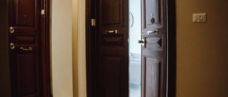 A hallway with wooden doors, a doormat, and a light fixture on the wall.