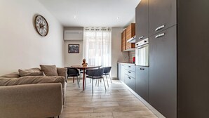 Un appartement moderne comprenant un coin repas, un canapé, une cuisine avec des meubles gris et une horloge murale.