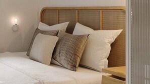 A bed with a woven headboard, multiple pillows, and a bedside table. - Veggera Living Tinos (Tinos)
