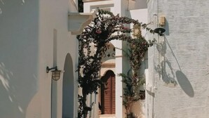 A narrow street with a white building featuring a bell tower and a cross on top. - Veggera Living Tinos (Tinos)