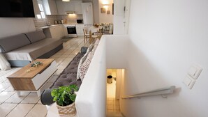 A modern kitchen with white cabinets, a dining area with a sofa and table, and a staircase leading to a lower level. - Villa THEA Myconian Vision Villas (C9GQ+Q6 Ελιά, Greece)