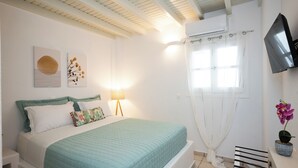 A bedroom with a bed, a TV, a window with curtains, and a wall-mounted TV. - Villa THEA Myconian Vision Villas (C9GQ+Q6 Ελιά, Greece)