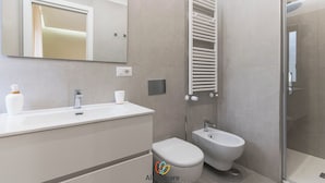 Un baño moderno con lavabo, espejo, inodoro y ducha.