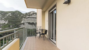 Un balcón con una mesa, sillas, un ventanal de vidrio y vistas a la montaña.