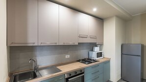 Una cocina con armarios de colores claros, un lavamanos de acero inoxidable, un microondas, una estufa y un refrigerador.