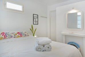 A hotel room with a bed, a wall-mounted mirror, a bedside table, and a window. - Apartment '- Ground Floor' with Balcony, Wi-Fi and Air Conditioning (Katápola)
