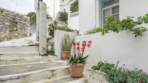 Ein weißes Gebäude mit einer Steinmauer und Stufen, die hinauf führen, dazu Kübel mit roten Blumen.