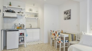Eine kompakte Küche mit Kühlschrank, Herd und Mikrowelle. Es gibt einen Essbereich mit Tisch und Stühlen, sowie ein Bett mit weißer Bettwäsche.