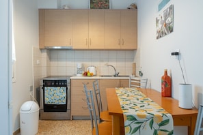 A kitchen with wooden cabinets, a stove, a sink, and a dining table with a fruit pattern tablecloth.