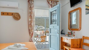 Ein Zimmer mit Bett, Schreibtisch, Stuhl, Fernseher und Blick auf Gebäude.