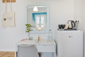 Pieni, siisti huone, jossa on valkoinen työpöytä, peili, viherkasvi, vedenkeitin ja jääkaappi.