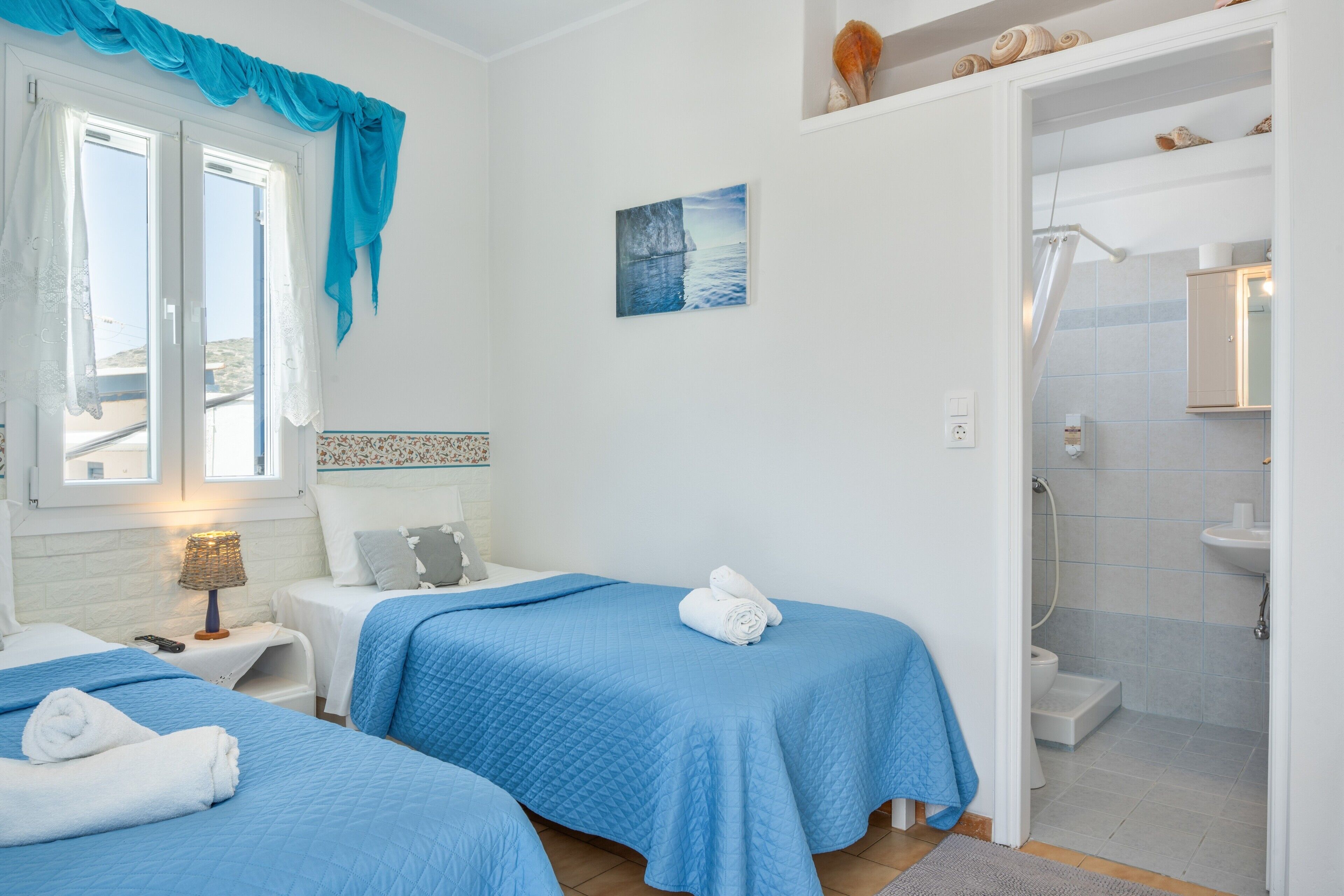A hotel room with two beds, a shower, and a view of the sea.