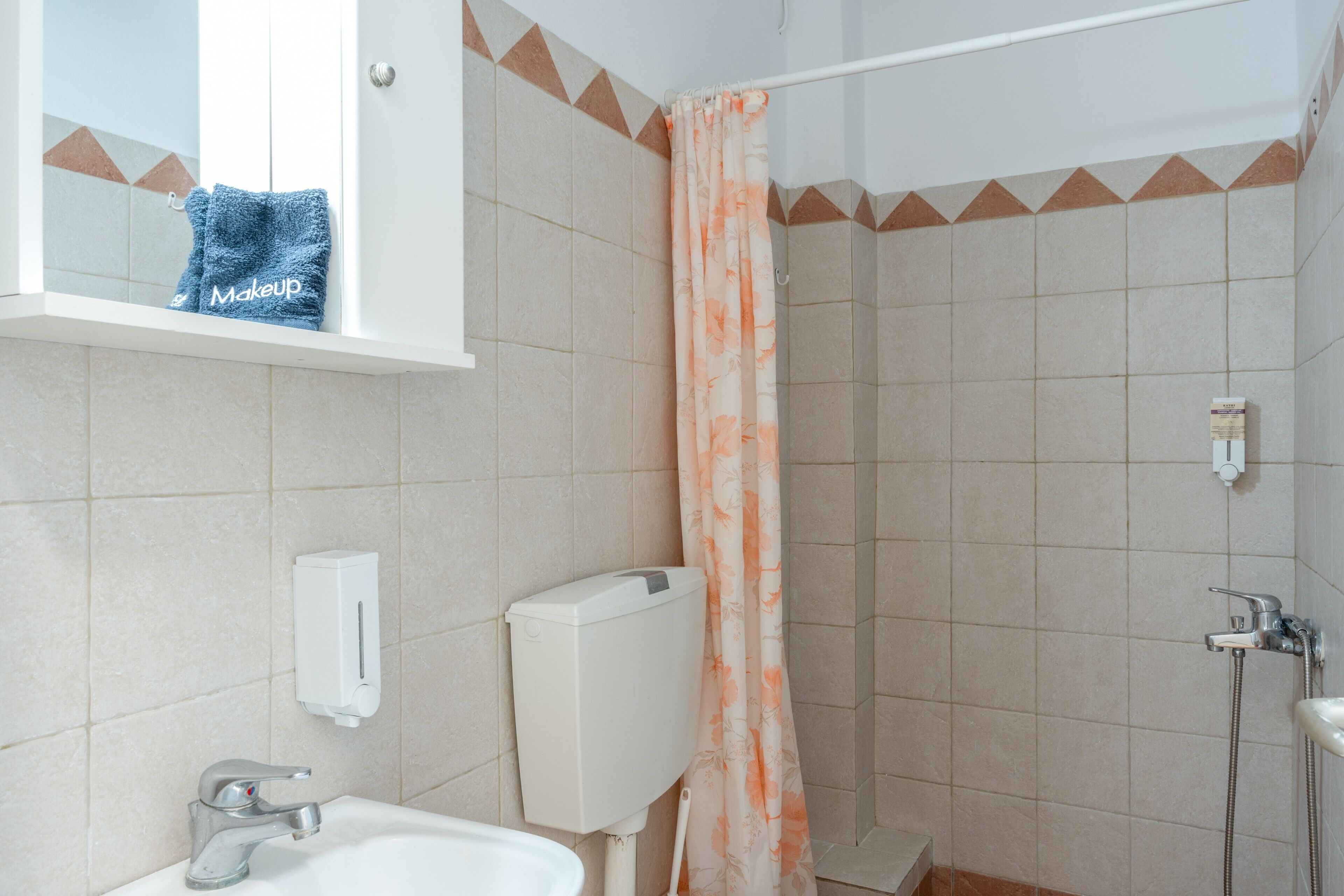 Ein Badezimmer mit Dusche, Waschbecken, Toilette, Handtuchhalter mit Handtuch und einer Seifenspender.