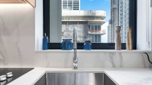 A modern kitchen with a stainless steel sink, a built-in stove, and a window overlooking a cityscape. - 2BR Near Bayside Market | Gym & Sauna (Miami)