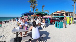 Un restaurant situé en bord de mer, avec une terrasse, des palmiers et un ciel d’un bleu éclatant.