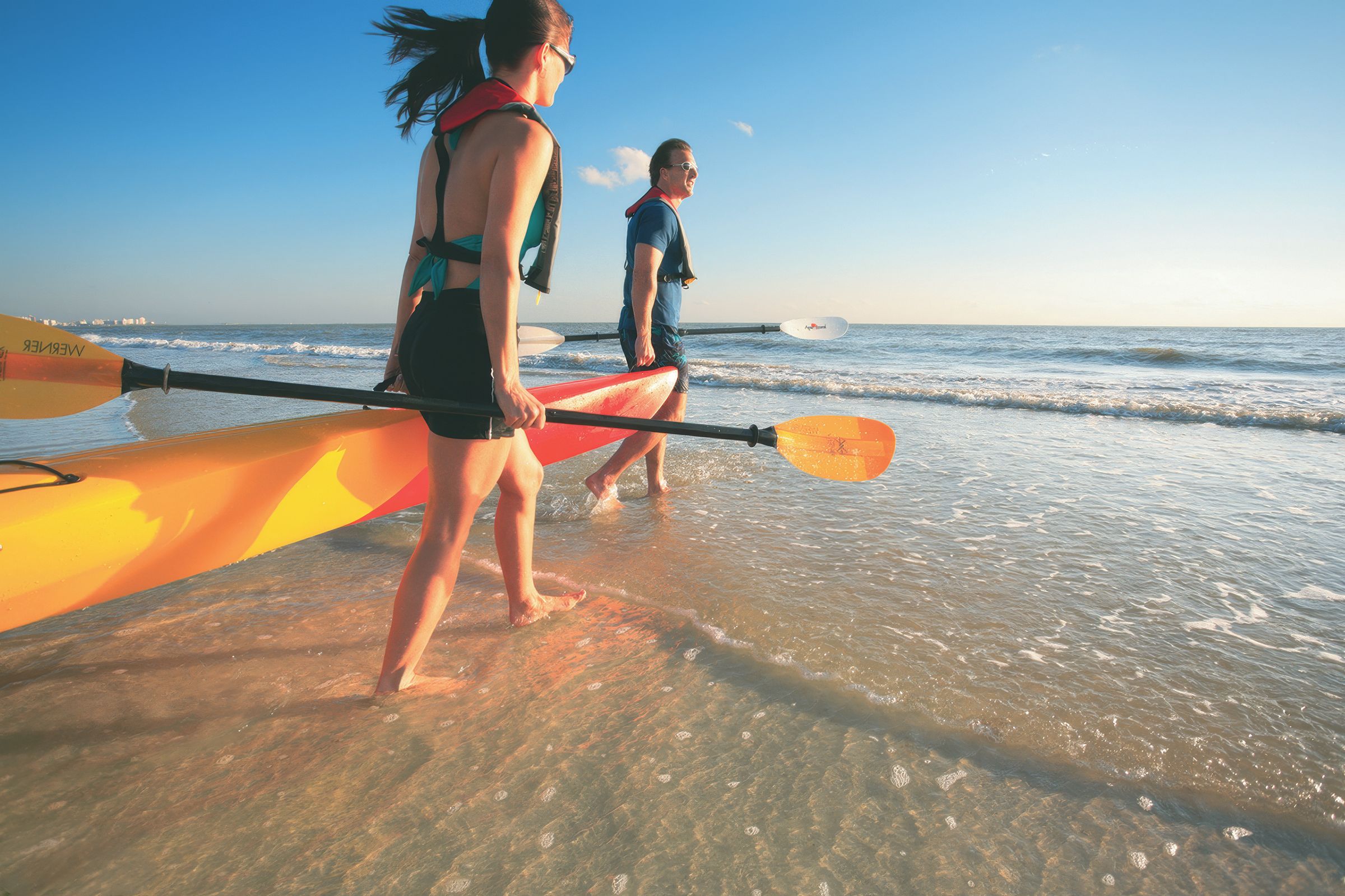 Two people walking on a beach with kayaks.