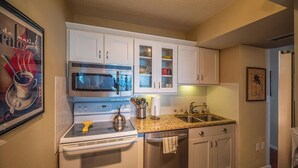 Une cuisine avec des armoires blanches, une cuisinière en acier inoxydable, un four à micro-ondes et un comptoir en granit.