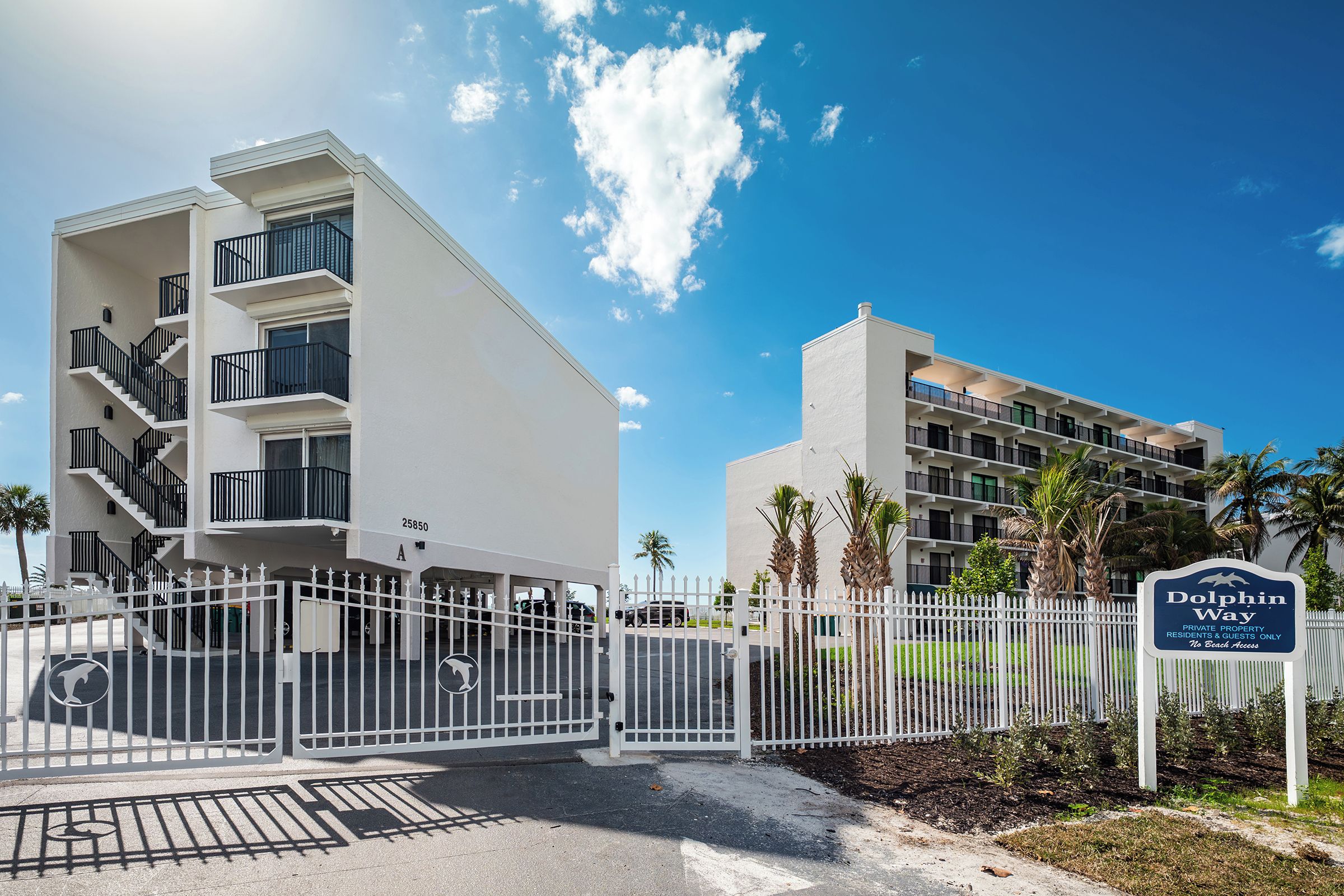 A gated private property with a sign indicating it is Dolphin Way, featuring a modern building with multiple balconies and a clear sky.