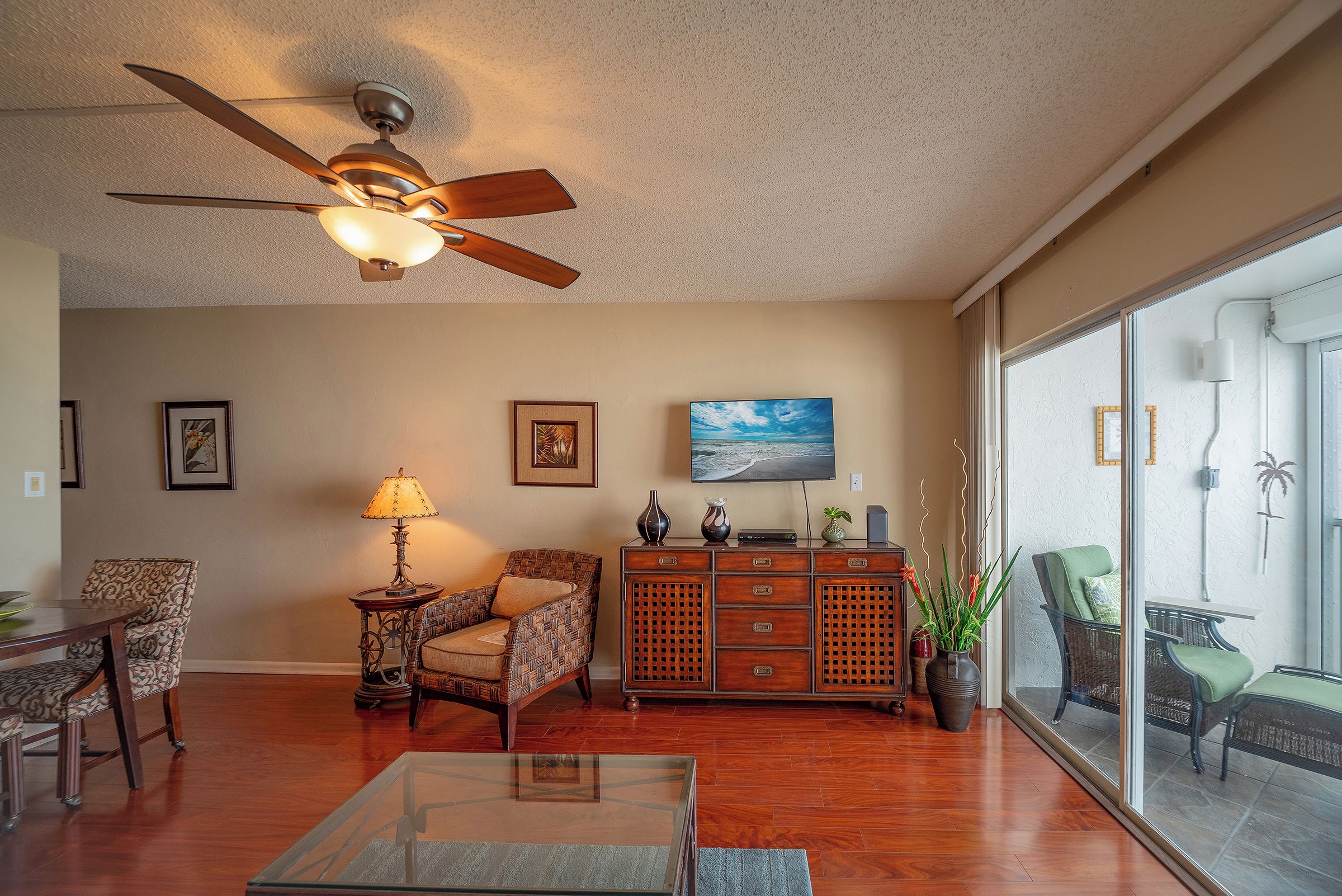 A living room with a ceiling fan, a television, a dining area with chairs, a coffee table, and a view through a large window.