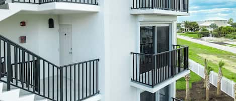 A multi-story residential building with balconies, a white exterior, and a view of a residential street.