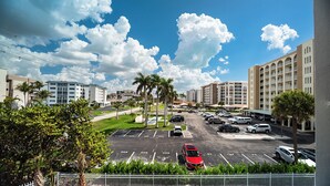 Un parking avec plusieurs voitures, des palmiers et des bâtiments en arrière-plan.