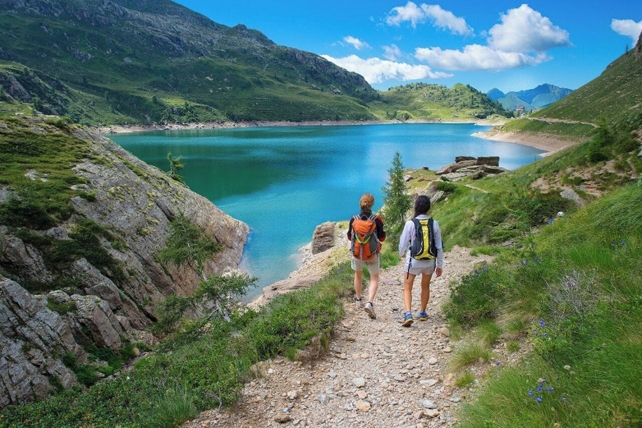 A mountain path leading to a lake with hikers.