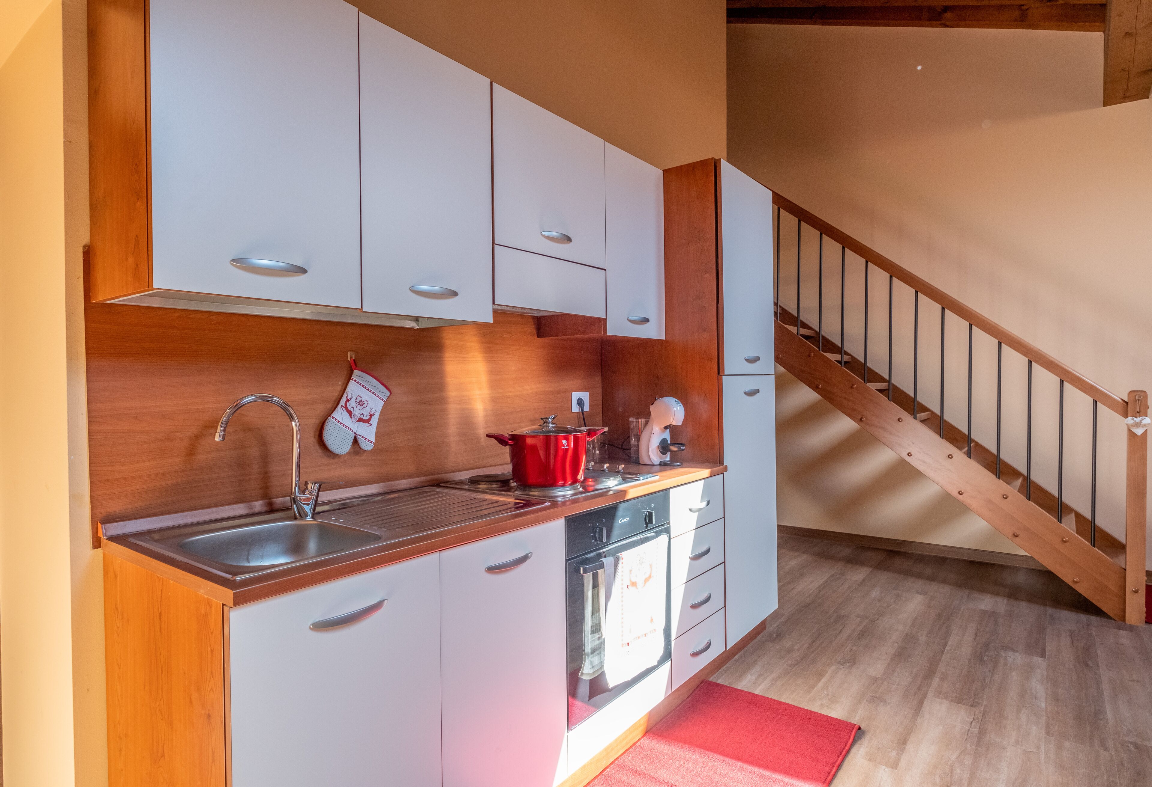 A compact kitchen with white cabinets, a wooden countertop, a stainless steel sink, and a built-in oven.