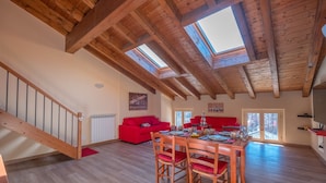 A spacious room with a wooden ceiling, skylights, a dining table with chairs, a red sofa, and a staircase. - Roncobellissimo! – Fresco e relax a 1.000 metri (Roncobello)