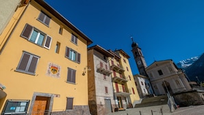 A street with buildings, a clock tower, and a mountain in the background. - Roncobellissimo! – Fresco e relax a 1.000 metri (Roncobello)