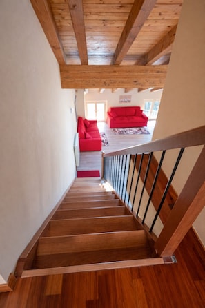 A wooden staircase leading to a red sofa in a well-lit room with a wooden ceiling.