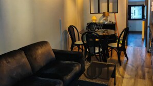 A living room with a black leather sofa, a coffee table, and a dining area with chairs and a table. - Furnished T2 apartment in a quiet villa in Mougins (Mougins)