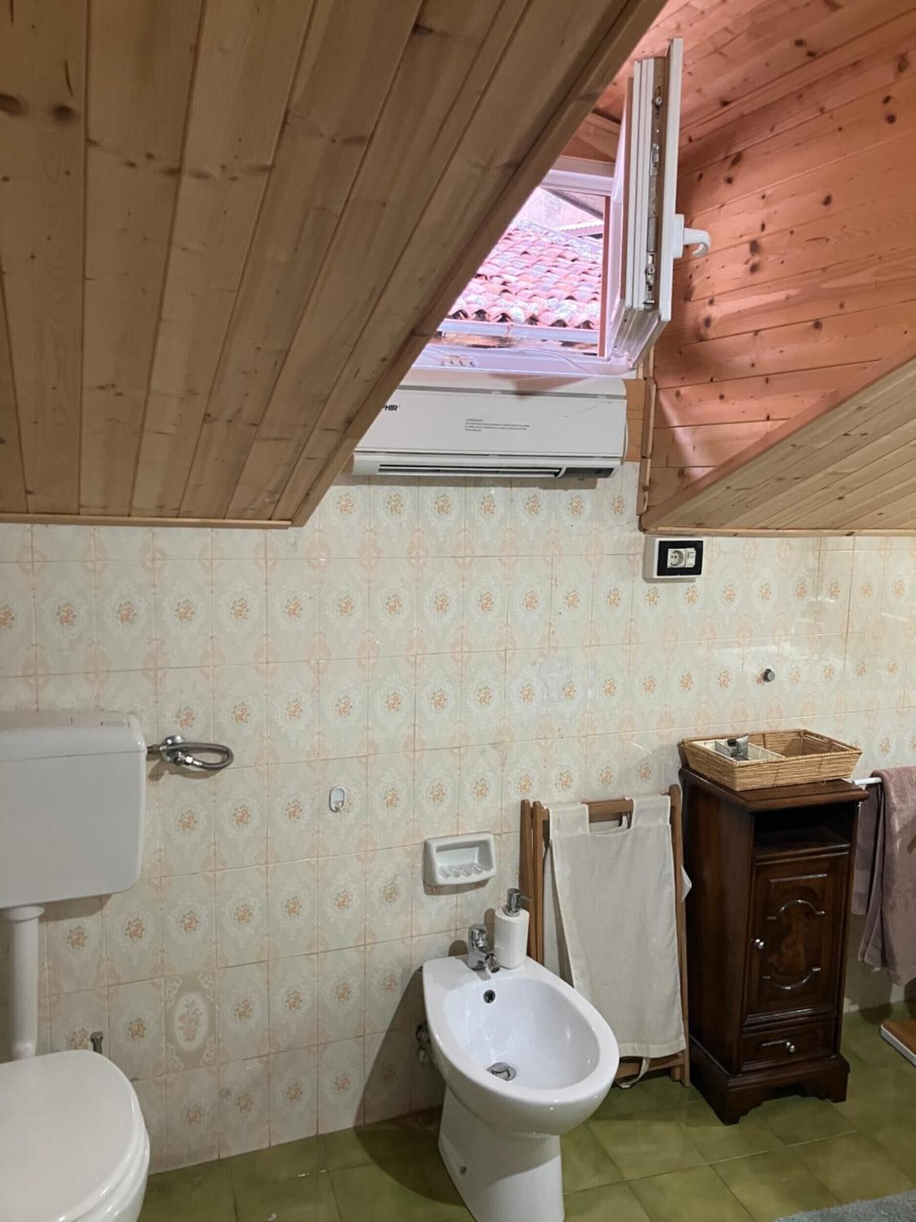 Ein Badezimmer mit Toilette, Bidet, Waschtisch und Fenster mit Klimaanlage darüber.