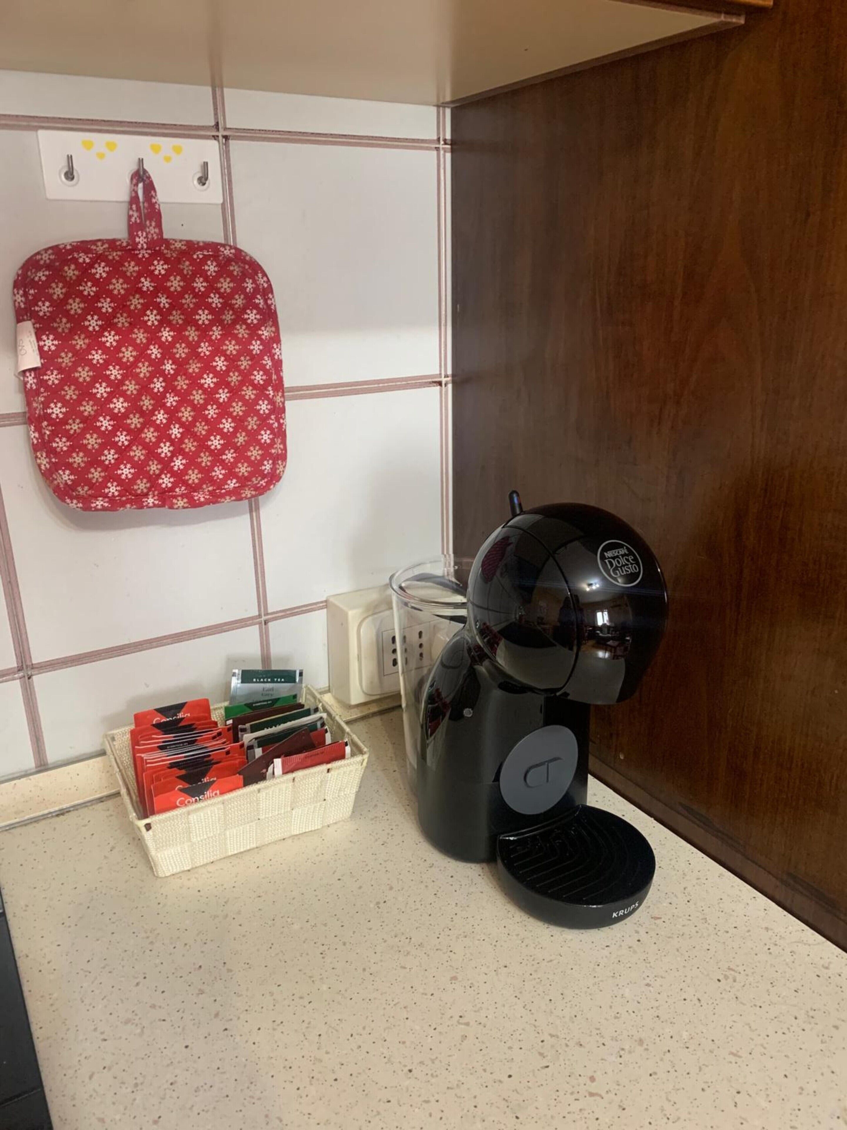 Una macchina da caffè, un cestino con capsule di caffè e una borsa rossa su un piano di lavoro piastrellato.