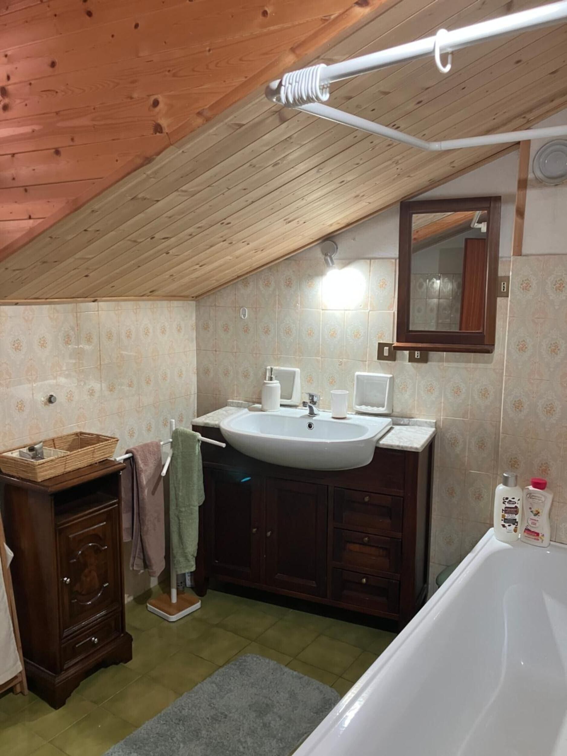 Ein kleines, gemütliches Badezimmer mit Holzbalkendecke, einem weißen Waschbecken, einem Spiegel und einer Badewanne.