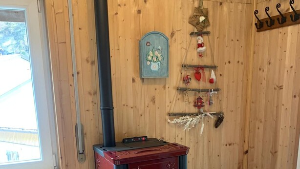 Huoneessa on puukamina, seinät ovat puuta, siellä on ikkuna ja hylly, jossa on esillä joulukoristeita.