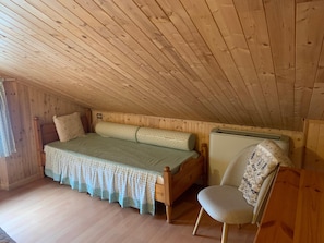 Ein kleiner, gemütlicher Raum mit Holzboden, einem Bett mit Musterdecke, einem Stuhl und einer Heizung.