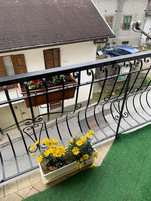 Ein Balkon mit Metallgeländer, einem Blumentopf und einer Blumenkiste mit gelben Blüten.
