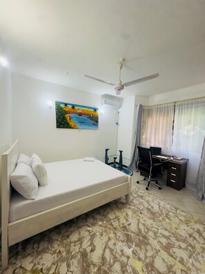 Een slaapkamer met een bed, bureau, stoel, airconditioning en een schilderij aan de muur.