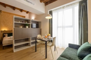A modern living room with a dining area, wooden beams, a sofa, and a TV on a shelf. - Cesariano, 11 - Stay on the bustling Cesariano Street (Milan)