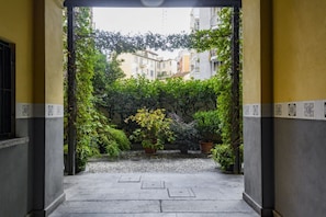 A courtyard with a pathway leading to a building entrance, surrounded by greenery and potted plants. - Cesariano, 11 - Stay on the bustling Cesariano Street (Milan)