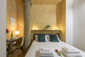 Ein Hotelzimmer mit Bett, Nachttischlampen, einem Schreibtisch mit Stuhl und einer Vase mit Blumen.
