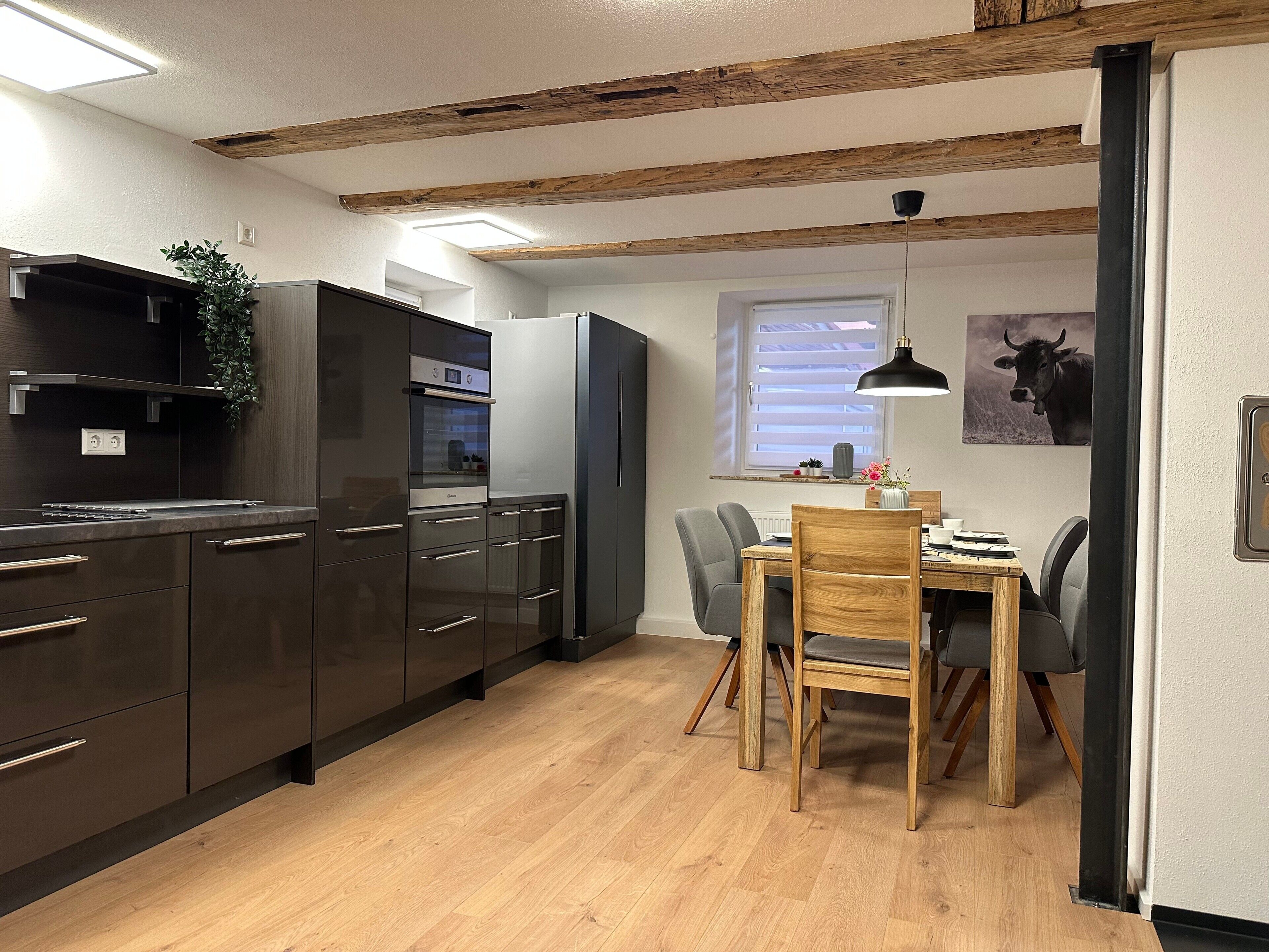 Eine moderne Küche mit dunklen Schränken, einem eingebauten Ofen und einem Essbereich mit einem Holztisch und Stühlen.