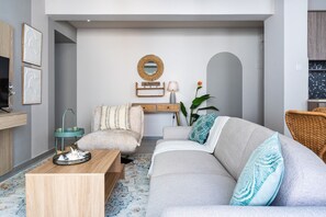 A modern living room with a grey sofa, a wooden coffee table, and a wicker chair. - Beach Daze 1-BR Apt By Finikoudes Beach (Larnaca)