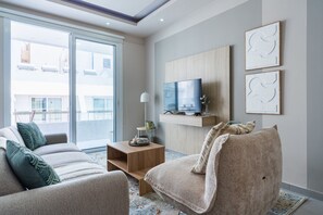 A modern living room with a sofa, armchair, TV, and artwork on the wall. - Beach Daze 1-BR Apt By Finikoudes Beach (Larnaca)