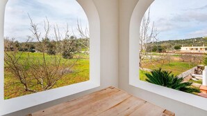 A room with two arched windows overlooking a grassy area with trees and a distant building. - Villa Badessa by Rentbeat (Ostuni)