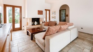 A living room with a sofa, coffee table, fireplace, and a view through a glass door. - Villa Badessa by Rentbeat (Ostuni)