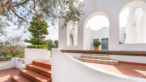 A white building with arched windows and a staircase leading to a door. - Villa Badessa by Rentbeat (Ostuni)