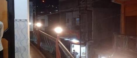 Μια νυχτερινή άποψη της εξωτερικής όψης ενός κτιρίου, με μεταλλική μπαλκονόπορτα, μια σκάλα και μια φωτεινή επιγραφή.
