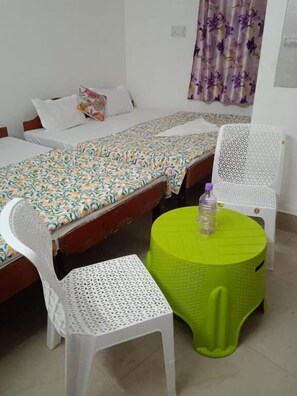 A room with two beds, a small round table with a chair, and a curtain with a floral pattern.