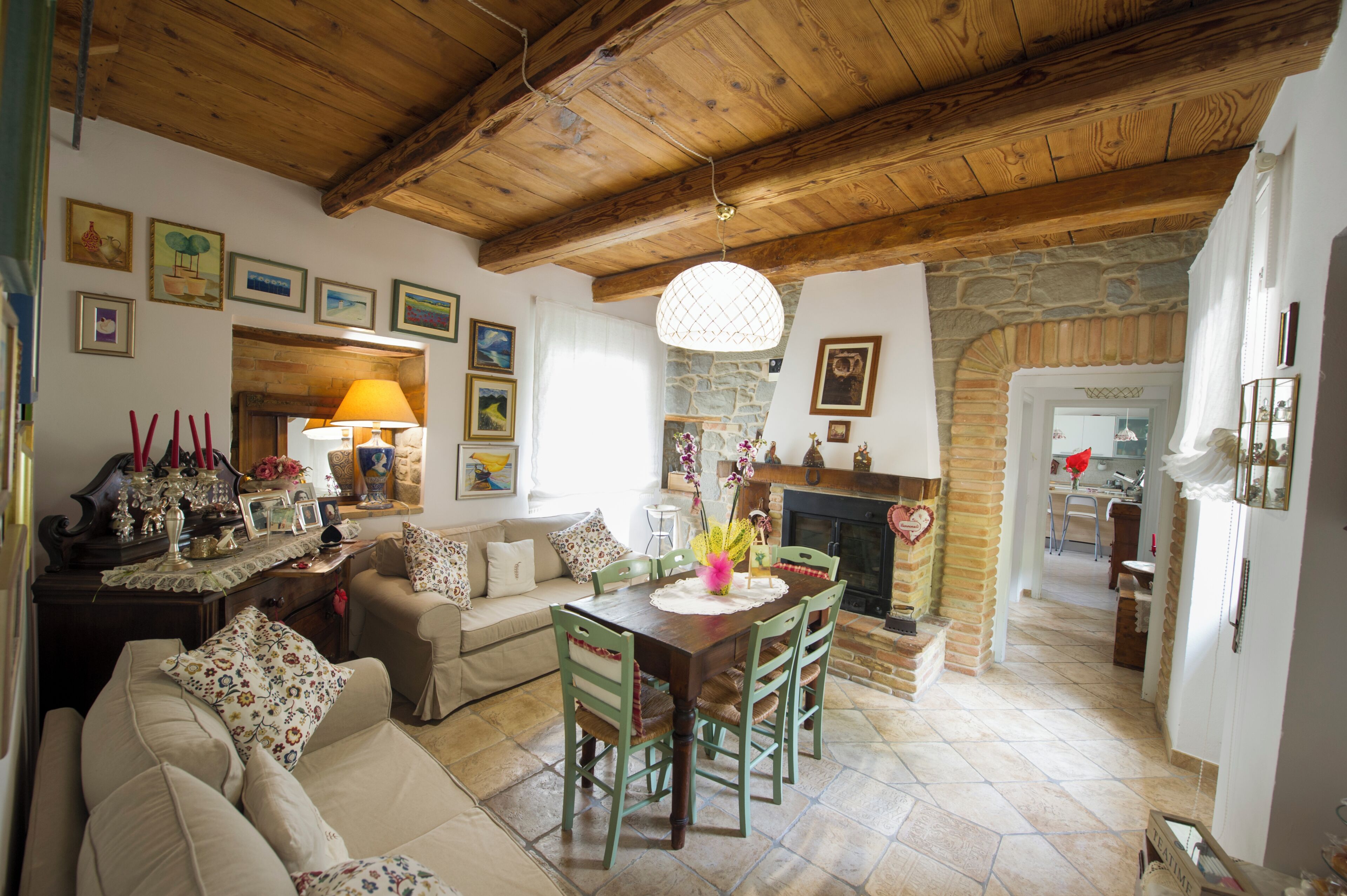 Ein gemütliches Wohnzimmer mit Holzbalkendecke, Kamin und Essbereich mit Tisch und Stühlen.